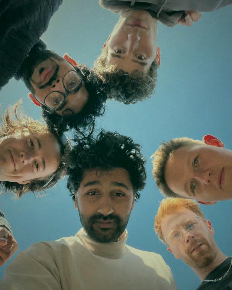 Seven of the team in a circle, photographed from below against a clear sky